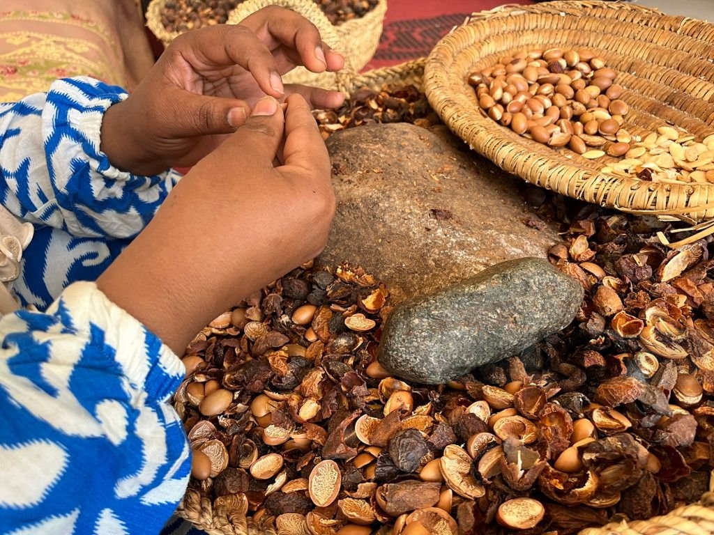 Hands cracking nuts by hand beside woven baskets of shelled kernels